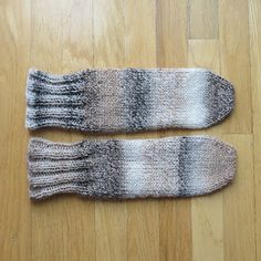 two gray and white knitted mittens sitting on top of a hard wood floor