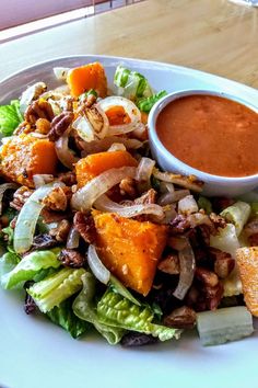 a white plate topped with salad and dressing next to a bowl of dipping sauce on top of it