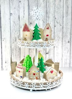 a three tiered cake with houses and trees on the top, in front of a wooden background