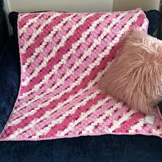 a pink and white crocheted blanket sitting on top of a blue couch next to a pillow