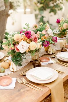 the table is set with plates, napkins and vases filled with colorful flowers