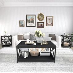 a living room with white couches and black coffee table in front of pictures on the wall