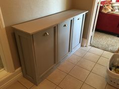 a cabinet in the corner of a room next to a dog bed and litter basket