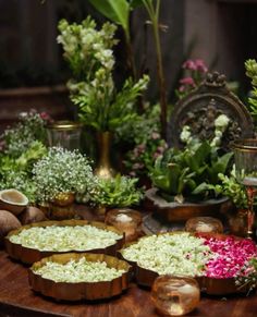 several bowls filled with flowers on top of a wooden table next to candles and vases