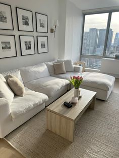 a living room with white couches and pictures hanging on the wall above it's coffee table