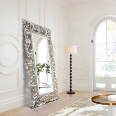 a large mirror sitting on top of a wooden floor next to a table with a lamp