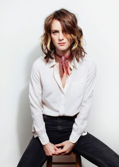 a woman sitting on top of a wooden stool wearing a white shirt and red tie