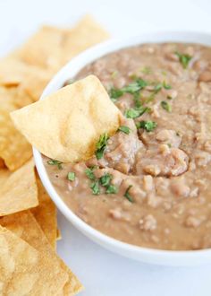 a white bowl filled with black bean dip surrounded by tortilla chips and cilantro