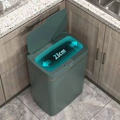 a green trash can sitting in the middle of a kitchen floor next to a sink