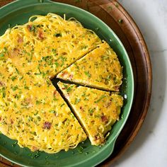 a green plate topped with an omelet covered in cheese and chives on top of a wooden tray