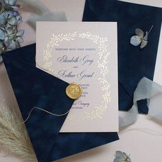 a wedding card with a wax stamp on it next to some blue envelopes and flowers