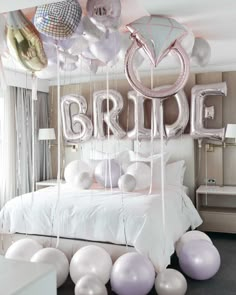 balloons are hanging from the ceiling in front of a bed with white sheets and pillows