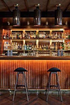 two stools sit in front of a bar with liquor bottles on the back wall