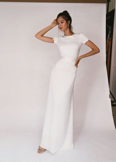 a woman standing in front of a white backdrop wearing a long dress with short sleeves