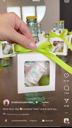 a person holding a green ribbon around a small box with some bottles in it on top of a table