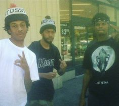 three young men standing next to each other in front of a store window with one holding up the peace sign