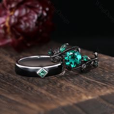 two rings with green stones sitting on top of a wooden table next to red flowers