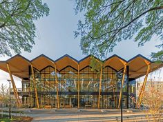 a large building with lots of glass and wood on the front, surrounded by trees