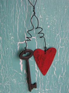 a red heart hanging from a hook with a key attached to it on a turquoise painted wall