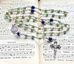 an open book with a rosary on it and music notes in the pages behind it