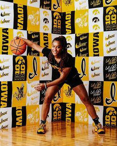 a young woman holding a basketball on top of a hard wood floor in front of a wall