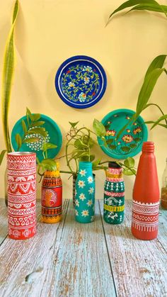 several colorful vases and plates on a wooden table with plants in the middle one has a green leafy plant