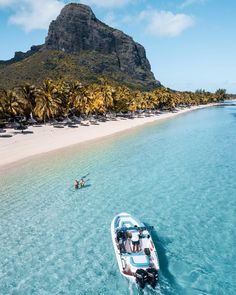 a small boat is in the clear blue water next to an island with palm trees