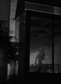 black and white photograph of a person standing in front of a building at night with his back to the camera