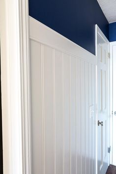 an empty room with blue walls and white paneling on the wall, in front of a door