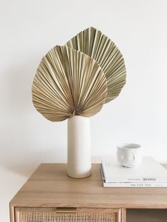 a white vase sitting on top of a wooden table next to a book and cup