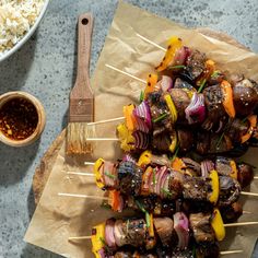 skewered meat and vegetables on wooden skewers next to bowl of rice