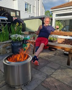 an older man sitting on a bench next to a fire pit and potted plants