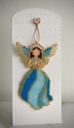 an angel ornament is hanging on a card with beadwork and thread