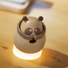 a small ceramic panda bear sitting on top of a wooden table next to a light