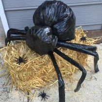 a large black spider statue sitting on top of hay covered ground next to a garage door