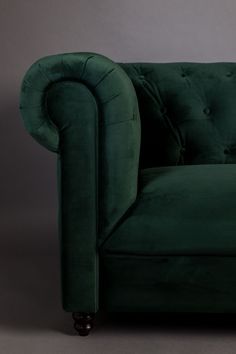 a green velvet couch with wooden legs and buttoned arms, in front of a gray background