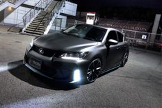 a dark colored car parked in front of some stairs at night with its lights on