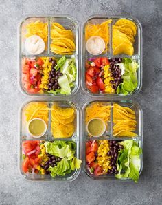 four plastic containers filled with salads and dressing on top of a gray countertop