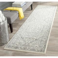 a white and gray area rug in a living room next to a grey bench with yellow throw pillows on it