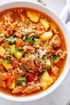 a white bowl filled with meat, vegetables and sauce on top of a table next to a napkin