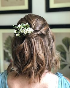 the back of a woman's head, with flowers in her hair and two framed pictures on the wall behind her