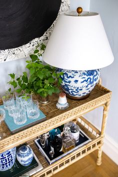 a wicker table with blue and white vases on it next to a lamp