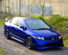 a blue car parked on the side of a dirt road next to a cement wall