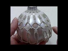 a hand holding a white ornament with beading on it's side