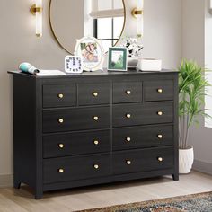 a black dresser with gold knobs in front of a mirror and potted plant