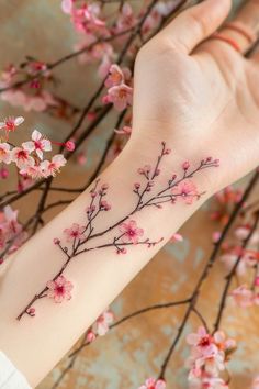 a woman's arm with pink flowers and branches tattooed on the left side of her arm