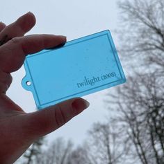 a person holding up a blue card with the words twilight zone on it in front of some trees