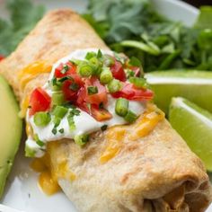 a burrito on a plate with avocado, tomatoes and cilantro