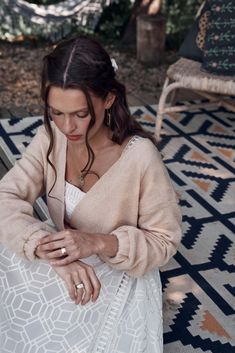 a woman sitting on top of a rug next to a chair and holding a cell phone