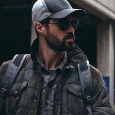 a man wearing sunglasses and a baseball cap walks down the street in front of a building